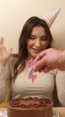 Bir kız elinde şenlikli bir pastayla masanın önünde oturuyor. 21 numaralı pastaya bir mum takılmış. Doğum günü kutlaması konsepti. dikey video
