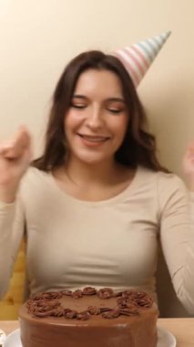 Bir kız elinde şenlikli bir pastayla bir masanın önünde oturur, 22 numara şeklinde bir mumla. Doğum günü kutlaması konsepti. dikey video