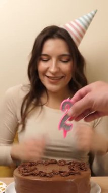 Bir kız elinde şenlikli bir pastayla bir masanın önünde oturuyor. 25 numaralı pastaya mum takılmış. Doğum günü kutlaması konsepti. dikey video