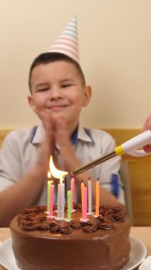 Çocuk elinde şenlikli bir pasta ve mumla bir masanın önünde oturur, onları söndürür ve hediyeler alır. Doğum günü kutlaması kavramı. dikey video