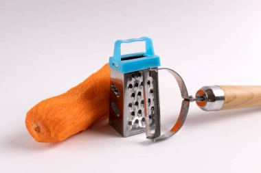 Soymak için bıçaklı çiğ havuç ve beyaz arka planda rendeleyici.