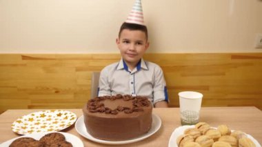 Bir çocuk elinde doğum günü pastası olan bir masanın önünde oturuyor, 7 numaralı şekle bürünmüş bir mum. Doğum günü kutlaması konsepti.