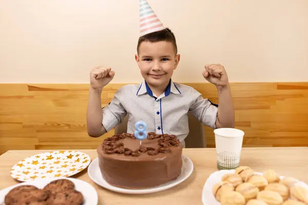 男の子がお祝いのケーキを持ってテーブルの前に座り そこでキャンドルが8の形で点灯しています 誕生日のお祝いのコンセプト ストック画像
