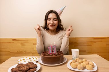 Masanın önünde elinde şenlikli bir pastayla oturan bir kız, içinde 17 numara şeklinde bir mum yakılıyor. Doğum günü kutlaması konsepti.