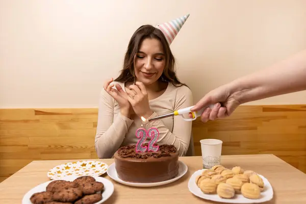 女の子は 22という数字の形でろうそくが点灯するお祝いのケーキでテーブルの前に座ります 誕生日のお祝いのコンセプト ストック写真