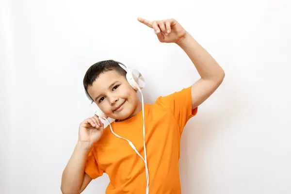 Beyaz arka planda turuncu tişörtlü bir çocuk duygusal olarak kulaklıkla müzik dinliyor..
