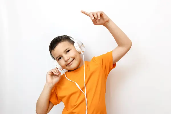 ホワイトバックグラウンドのオレンジTシャツの男の子は感情的にヘッドフォンで音楽をリストします ストック写真