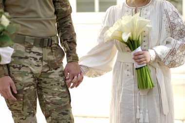 Genç bir çift. Askeri üniformalı damat ve beyaz çiçekli nakışlı gelinlik içinde gelin..