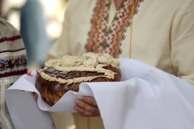 Nakışlı gömlekli bir adam elinde bir düğün somunu tutuyor..