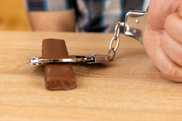 Человек прикован наручниками к плитке шоколада. Концепция сладкой зависимости.