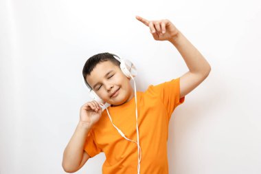Beyaz arka planda turuncu tişörtlü bir çocuk duygusal olarak kulaklıkla müzik dinliyor..