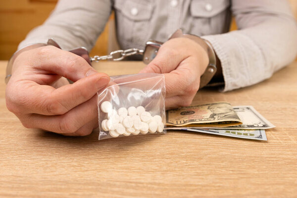 Woman in handcuffs with medicine and dollars. The concept of drug addiction. Drug crime.