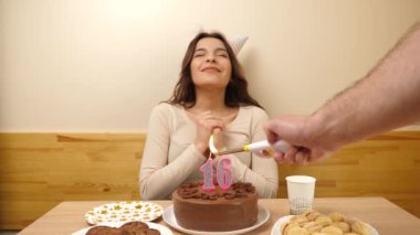 Kız elinde şenlikli bir pastayla bir masanın önünde oturuyor, içinde 16 numara şeklinde bir mum yanıyor ve söndürüyor. Doğum günü kutlaması kavramı. Yavaş çekim
