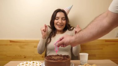 Kız elinde şenlikli bir pastayla bir masanın önünde oturuyor, 19 numara şeklinde bir mum yanıyor ve o da söndürüyor. Doğum günü kutlaması kavramı. Yavaş çekim