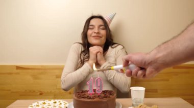 Kız elinde şenlikli bir pastayla bir masanın önünde oturuyor, 19 numara şeklinde bir mum yanıyor ve o da söndürüyor. Doğum günü kutlaması kavramı. Yavaş çekim
