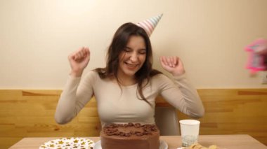 Masanın önünde elinde şenlikli bir pastayla oturan bir kız. 17 numaralı pastaya mum takılmış. Doğum günü kutlaması konsepti. Yavaş çekim