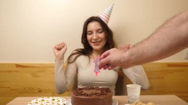 Bir kız elinde şenlikli bir pastayla masanın önünde oturuyor. 18 numaralı pastaya mum takılmış. Doğum günü kutlaması konsepti. Yavaş çekim