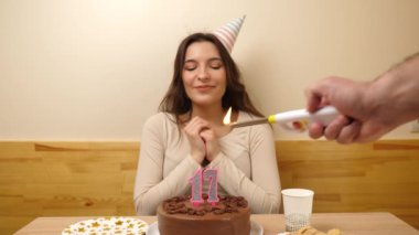Kız elinde şenlikli bir pastayla bir masanın önünde oturuyor. 17 numara şeklinde bir mum yanıyor ve o da söndürüyor. Doğum günü kutlaması kavramı. Yavaş çekim