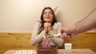Kız elinde şenlikli bir pastayla bir masanın önünde oturuyor. 21 numara şeklinde bir mum yanıyor ve söndürüyor. Doğum günü kutlaması kavramı. Yavaş çekim