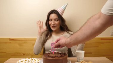 Bir kız elinde şenlikli bir pastayla masanın önünde oturuyor. 21 numaralı pastaya bir mum takılmış. Doğum günü kutlaması konsepti. Yavaş çekim