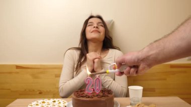 Kız elinde şenlikli bir pastayla bir masanın önünde oturuyor, 20 numara şeklinde bir mum yanıyor ve o da söndürüyor. Doğum günü kutlaması kavramı. Yavaş çekim