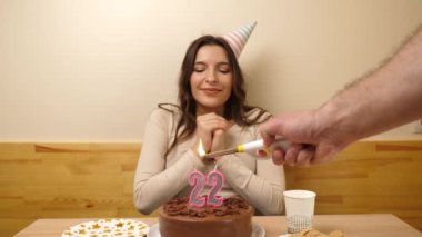 Kız elinde şenlikli bir pastayla bir masanın önünde oturuyor, 22 numara şeklinde bir mum yanıyor ve söndürüyor. Doğum günü kutlaması kavramı. Yavaş çekim