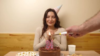Kız elinde şenlikli bir pastayla bir masanın önünde oturuyor, içinde 24 numara şeklinde bir mum yanıyor ve söndürüyor. Doğum günü kutlaması kavramı. Yavaş çekim
