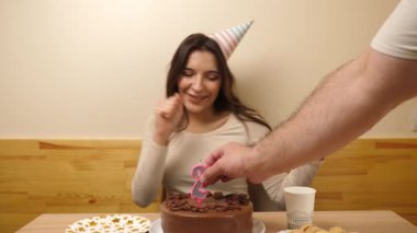 Bir kız elinde şenlikli bir pastayla bir masanın önünde oturuyor. 25 numaralı pastaya mum takılmış. Doğum günü kutlaması konsepti. Yavaş çekim