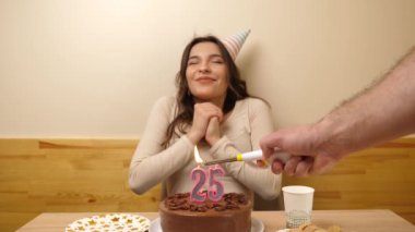 Kız elinde şenlikli bir pastayla bir masanın önünde oturuyor, içinde 25 numara şeklinde bir mum yanıyor ve söndürüyor. Doğum günü kutlaması kavramı. Yavaş çekim