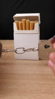Bir kadın bir paket sigaraya kelepçelendi. Tütün bağımlılığı konsepti. Sigara içmek utanç verici. Dikey video