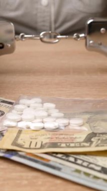İlaç ve dolarlarla kelepçelenmiş bir kadın. Uyuşturucu bağımlılığı kavramı. Uyuşturucu suçu. Dikey video
