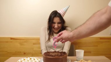 Bir kız elinde şenlikli bir pastayla bir masanın önünde oturuyor, 27 numara şeklinde bir mumla. Doğum günü kutlaması konsepti. Yavaş çekim