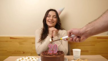 Kız elinde şenlikli bir pastayla bir masanın önünde oturuyor. 29 numara şeklinde bir mum yanıyor ve söndürüyor. Doğum günü kutlaması kavramı. Yavaş çekim