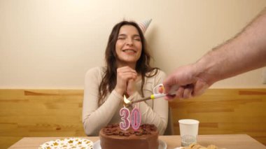 Kız elinde şenlikli bir pastayla bir masanın önünde oturuyor, içinde 30 numara şeklinde bir mum yanıyor ve söndürüyor. Doğum günü kutlaması kavramı. Yavaş çekim