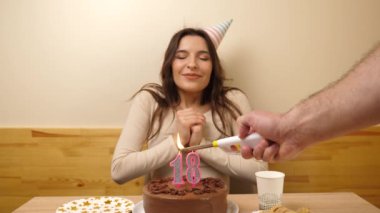 Kız elinde şenlikli bir pastayla bir masanın önünde oturuyor. 18 numara şeklinde bir mum yanıyor ve söndürüyor. Doğum günü kutlaması kavramı. Yavaş çekim