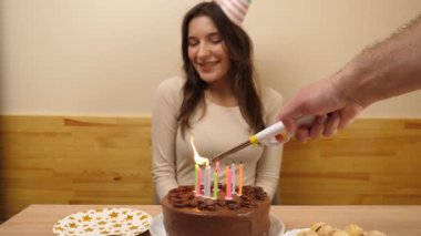 Kız elinde mumların yakıldığı şenlikli bir pastayla masanın önünde oturuyor. Doğum günü kutlaması kavramı. Yavaş çekim