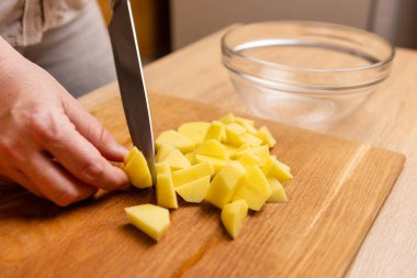 Çiğ patatesler bıçakla küp şeklinde kesilir. Sebze yemeği hazırlama.