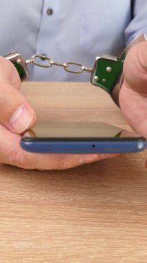 Akıllı telefonlu kelepçeli bir adam. Akıllı telefon bağımlılığı. Dikey video.