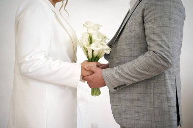 Yeni evliler bir buket beyaz kaala ile el ele tutuşuyorlar. Düğün töreni..