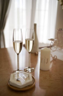 Köpüklü şarap kadehleri, alyanslar ve masada bir mum. Düğün hazırlıkları..