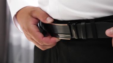 Adam belindeki kemeri sıkıyor. Şık erkek aksesuarları..