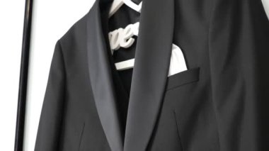 Duvardaki beyaz askıda siyah bir erkek kıyafeti asılı. Şenlikli erkek kıyafetleri.