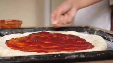 Sos pizzanın tabanına uygulanır. Ev yapımı pizza..