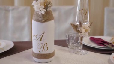 Şenlik masasında yeni evlilerin baş harflerinin yazılı olduğu bir şişe şarap var. Düğün gelenekleri..