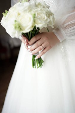 Parmağında alyansı olan gelinlik giymiş gelin elinde bir buket çiçek tutuyor. Düğün hazırlıkları..         