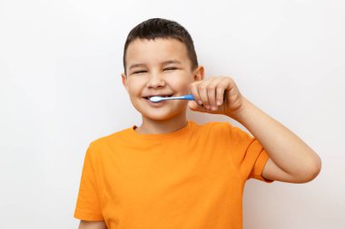 Turuncu tişörtlü bir çocuk gülümseyerek dişlerini fırçalıyor..