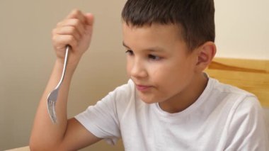 Çocuk masada oturuyor ve çatalla erişte yiyor..