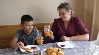 Anne ve oğlu masada oturmuş, yemek yiyor ve içki içiyorlar..