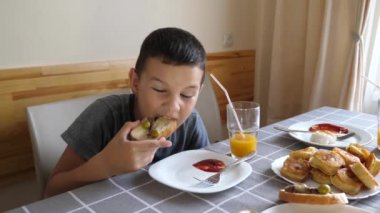 Çocuk masada oturuyor, yemek yiyor ve meyve suyu içiyor..