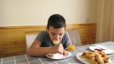 Çocuk masada oturuyor, yemek yiyor ve meyve suyu içiyor..